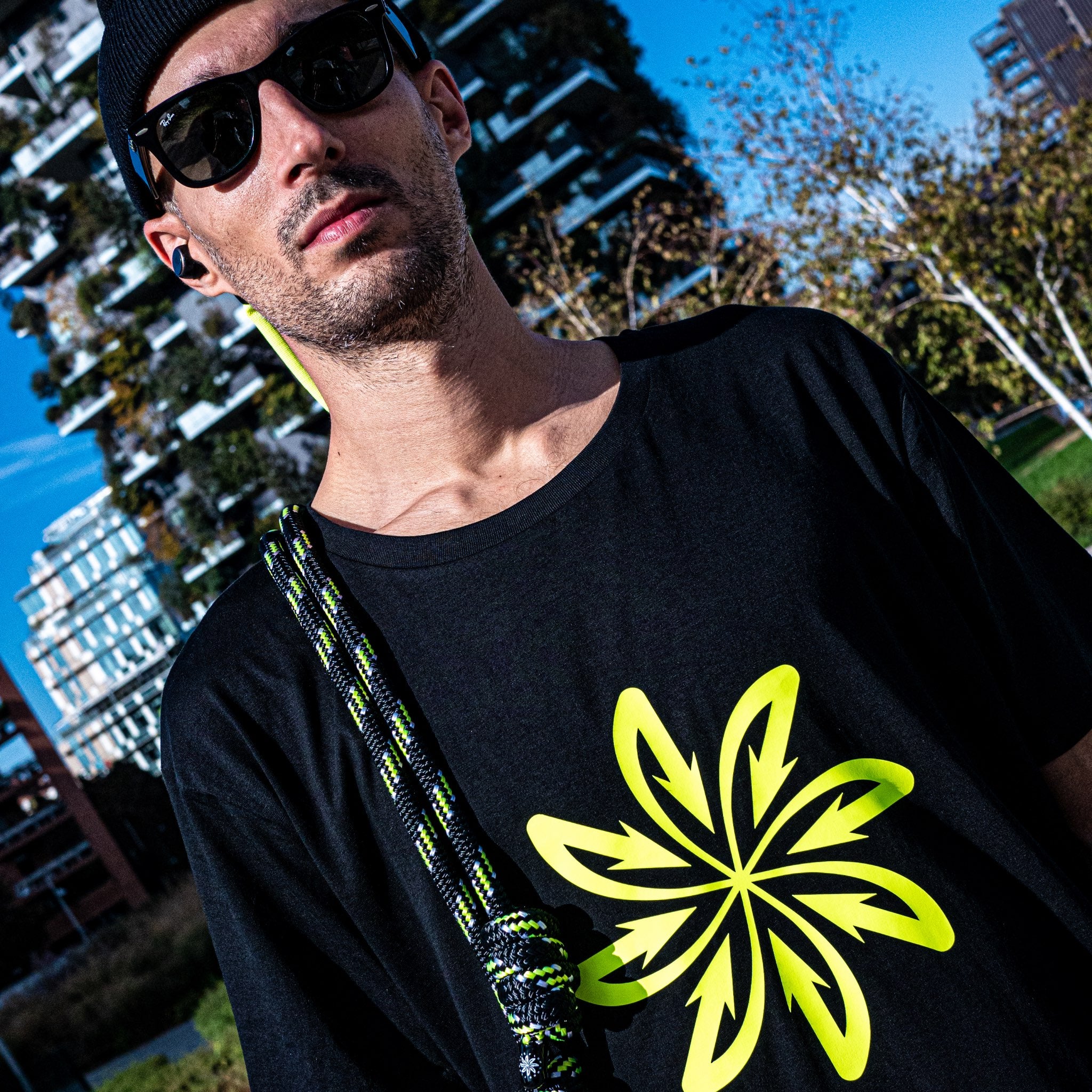 Phil standing wearing his black t-shirt with yellow fluo logo and with his Good Flow Milano Court SP rope over his shoulder, with Milan's Bosco Verticale in the background.